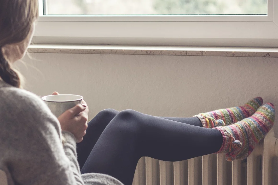 Person mit Tasse an Heizung